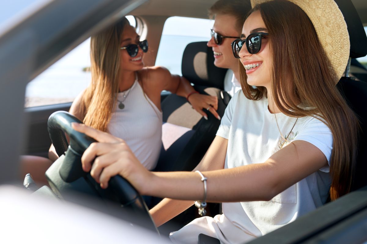 Two women wearing sunglasses and hats driving convertible car together, smiling.