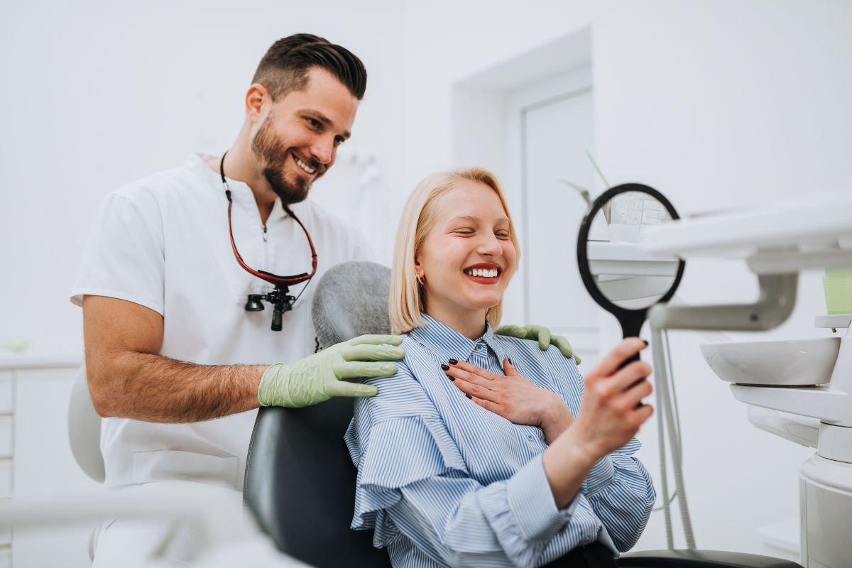 Dentist showing young patient mirror in bright dental office examining teeth.