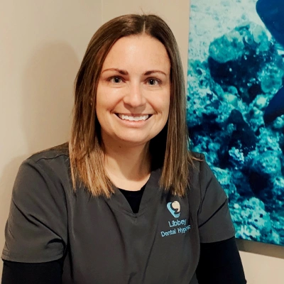 Professional woman smiling at camera wearing dark scrubs with coral reef photo in background.