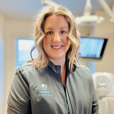 Professional woman in medical scrubs smiling at dental office reception area.