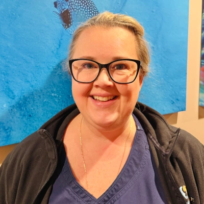 Woman with glasses smiling at camera against blue background in indoor setting.