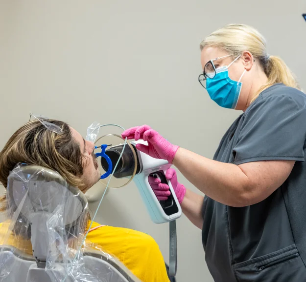Dental assistant taking a digital X-ray of a patient with a handheld scanner